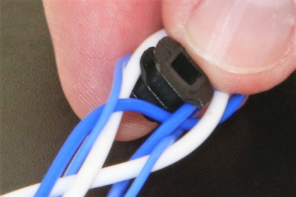 A finger is seen pushing a spacer into the loop of a tunable audio cable so altering the loop's dimensions and thereby its electrical characteristics